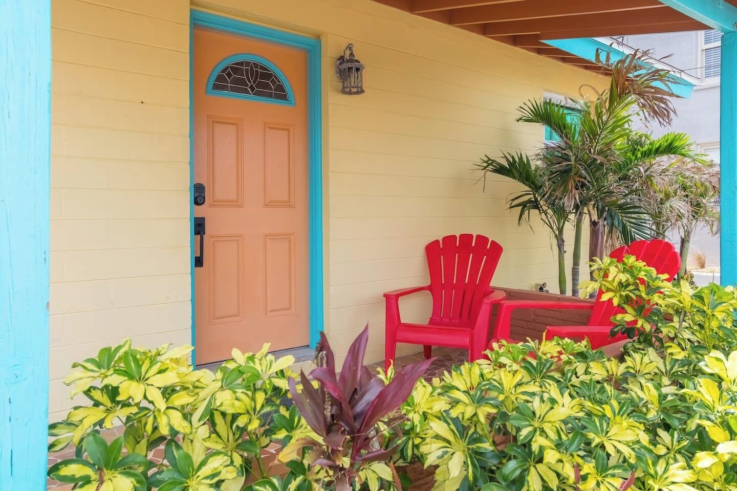 A building with a yellow exterior and a blue door. There are red chairs and a small table outside.