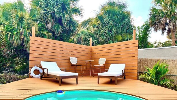 A wooden deck with a swimming pool, two lounge chairs, and a table with chairs. - Cowboy Pool / Mini Golf / Walk 2 Beach & Ocean Center! Pets OK (Daytona Beach)
