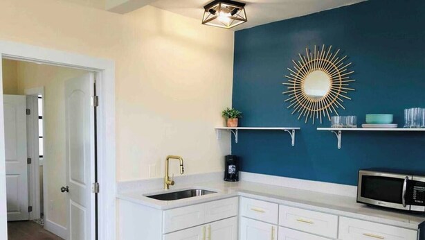 Une cuisine moderne avec des meubles blancs, un mur d’accent bleu, un miroir à cadre doré et un four à micro-ondes.