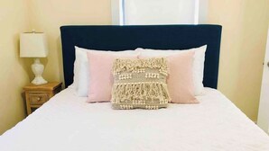 Un lit bien fait, avec une tête de lit sombre, deux oreillers et un couvre-lit décoratif.
