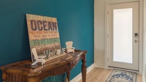 Un mur de couleur turquoise orné d’une enseigne en bois sur laquelle on peut lire « LEÇONS DE L’OCÉAN », ainsi qu’une console en bois accompagnée de chaises.