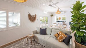 A living room with a sofa, a hanging plant, a ceiling fan, and a dining area with chairs and a table.