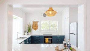 A modern kitchen with white cabinetry, a central island, a hanging light fixture, and a window with blinds.