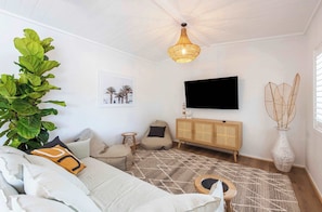 Un salon comprenant un canapé, un fauteuil poire, un téléviseur, un meuble en bois, une grande plante et un tapis à motifs.
