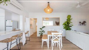A modern kitchen with white cabinetry, a built-in refrigerator, and a dining area with white chairs and a wooden table.