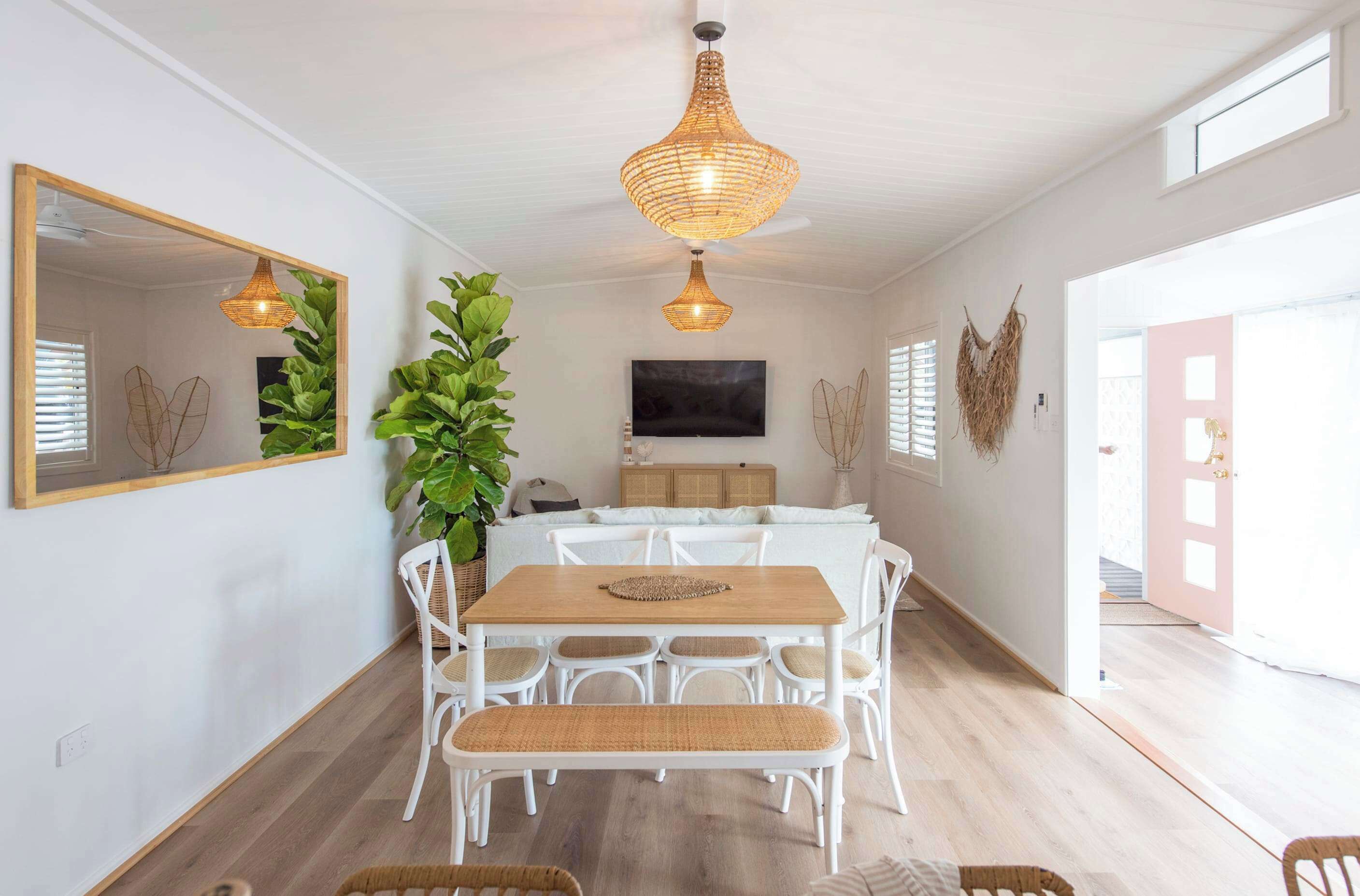 Un espace repas avec une table en bois, des chaises blanches et un luminaire suspendu au plafond, fait de fibres tressées.