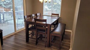 Un área de comedor con una mesa y sillas de madera, ventanas amplias y vista a una terraza nevada.