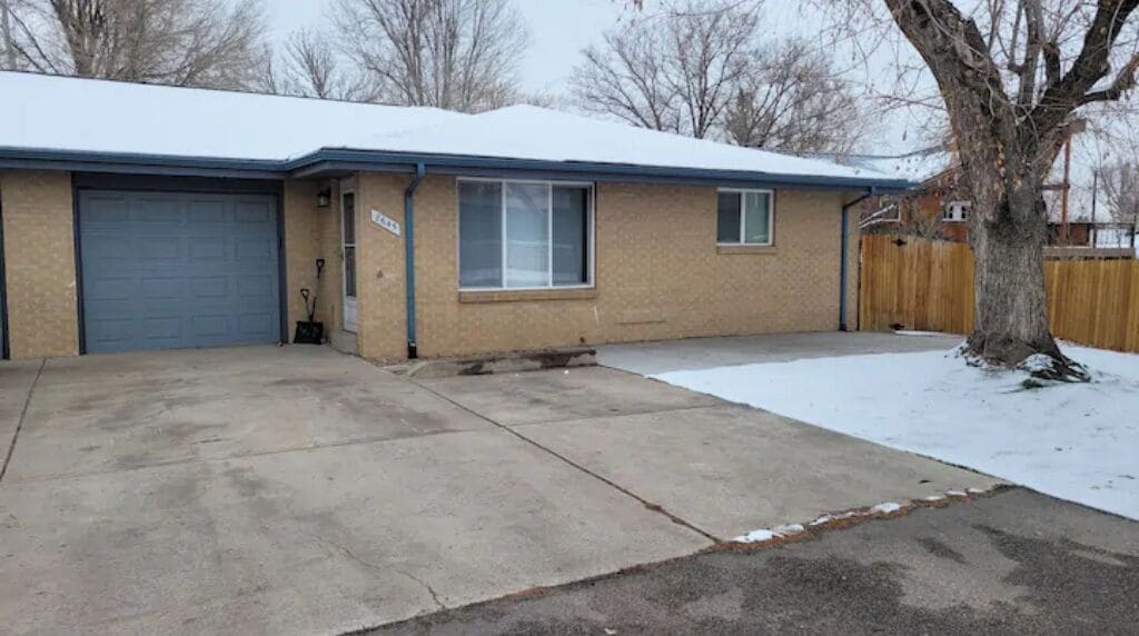 A single-story house with a garage, a front yard with snow, and a wooden fence.