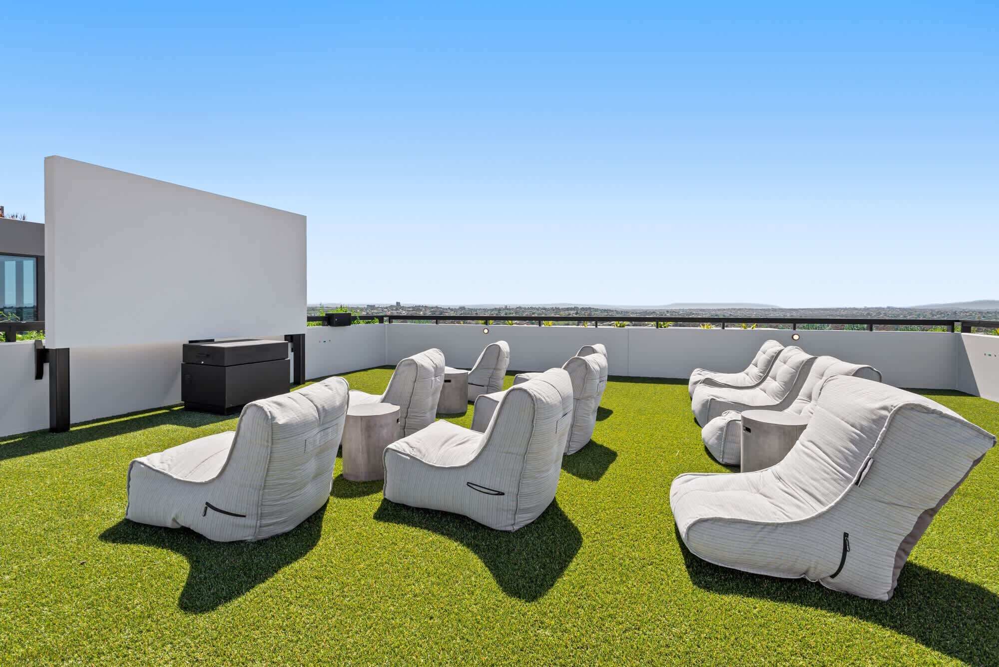 A rooftop terrace with white cushioned seating and a small table, surrounded by artificial grass.