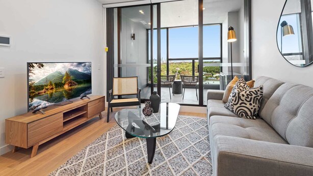Een moderne woonkamer met een flatscreen televisie, een glazen salontafel, een bank en een balkon met uitzicht.