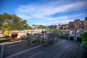A rooftop terrace with wooden furniture, potted plants, and a view of the cityscape. - New York-Style Loft in Sydney CBD with City Views (Darlinghurst)