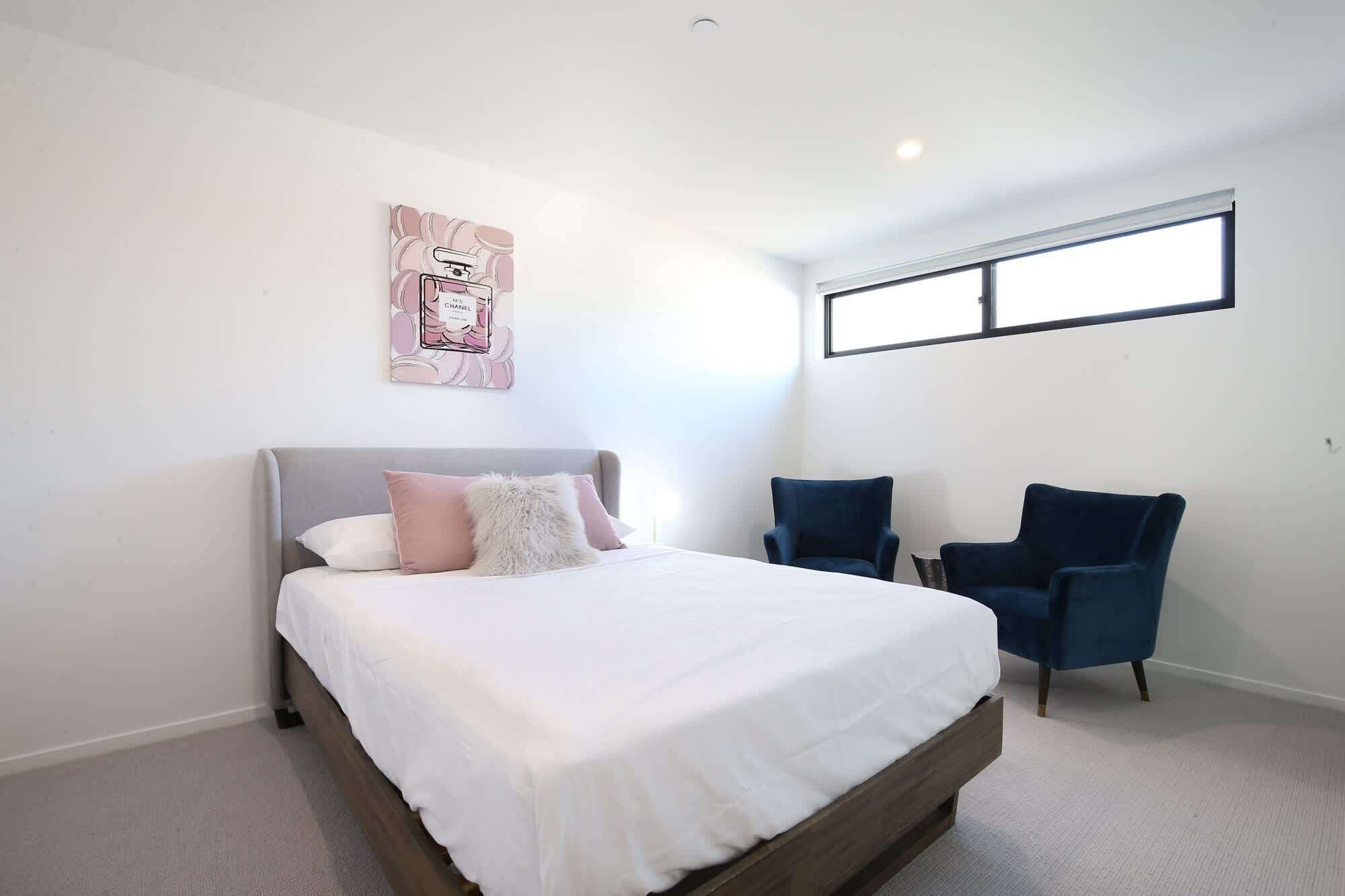 Une chambre à coucher comprenant un lit, deux chaises, une fenêtre et une œuvre d’art murale.