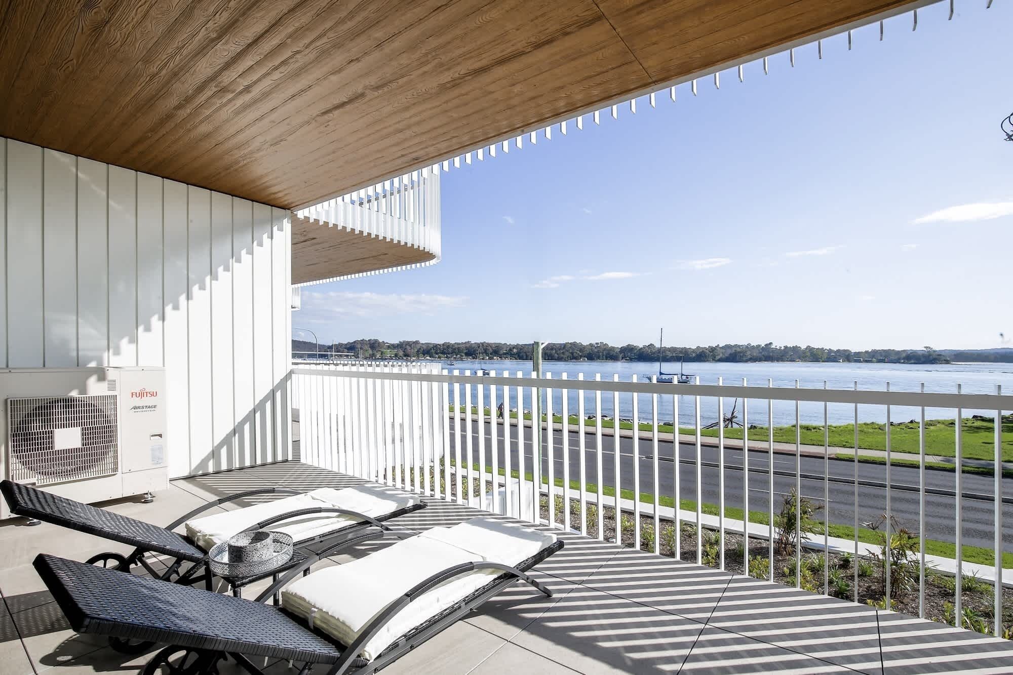 Ein Balkon mit Sitzgelegenheit im Freien, Blick auf ein Gewässer und eine weiße Brüstung.