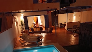 Une piscine avec des chaises longues, un espace repas avec des tables et des chaises, et un mur en pierre.
