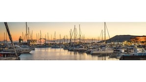Un port de plaisance où sont amarrés de nombreux bateaux, un phare en arrière-plan et un paysage urbain avec des bâtiments.