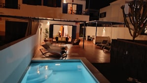 Un espace piscine avec des chaises longues et un coin repas avec des tables et des chaises.