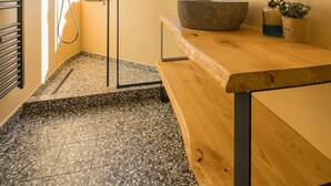 Une salle de bain moderne avec une baignoire sur pieds, un meuble-lavabo en bois, un grand miroir et une fenêtre laissant entrer la lumière naturelle.