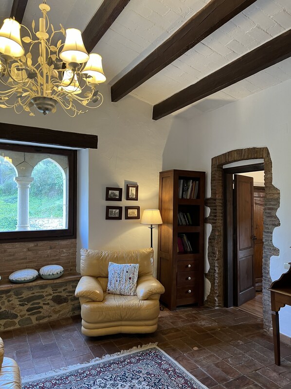 Ein gemütliches Wohnzimmer mit Ledersessel, einer Chandelüster, einem Bücherregal und einer Steinwand.