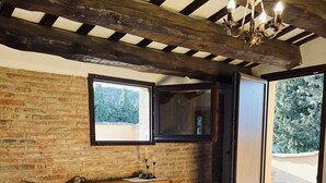 Ein rustikales Zimmer mit zwei Betten, einer Holzkommode, einem Korbsessel und einem großen Fenster mit Blick auf Bäume.