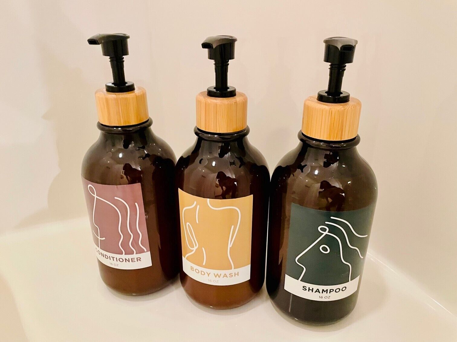 Tres botellas de jabón líquido con dispensadores, cada una etiquetada para un uso diferente: acondicionador, gel de baño y champú.