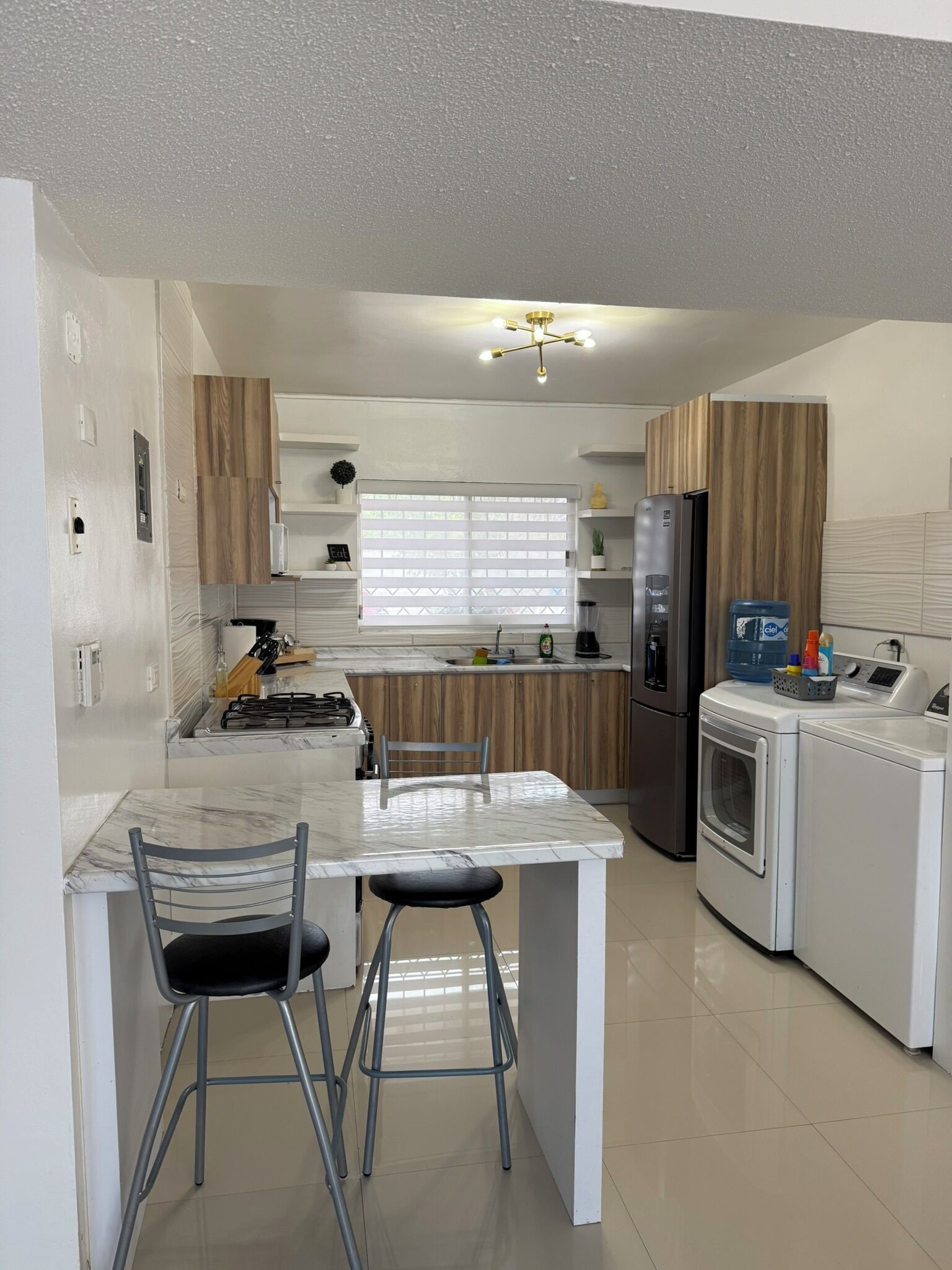 A compact kitchen with a central island, a refrigerator, a washing machine, and a dining area with two chairs.