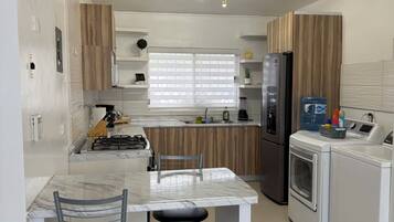 A compact kitchen with a central island, a refrigerator, a washing machine, and a dining area with two chairs.