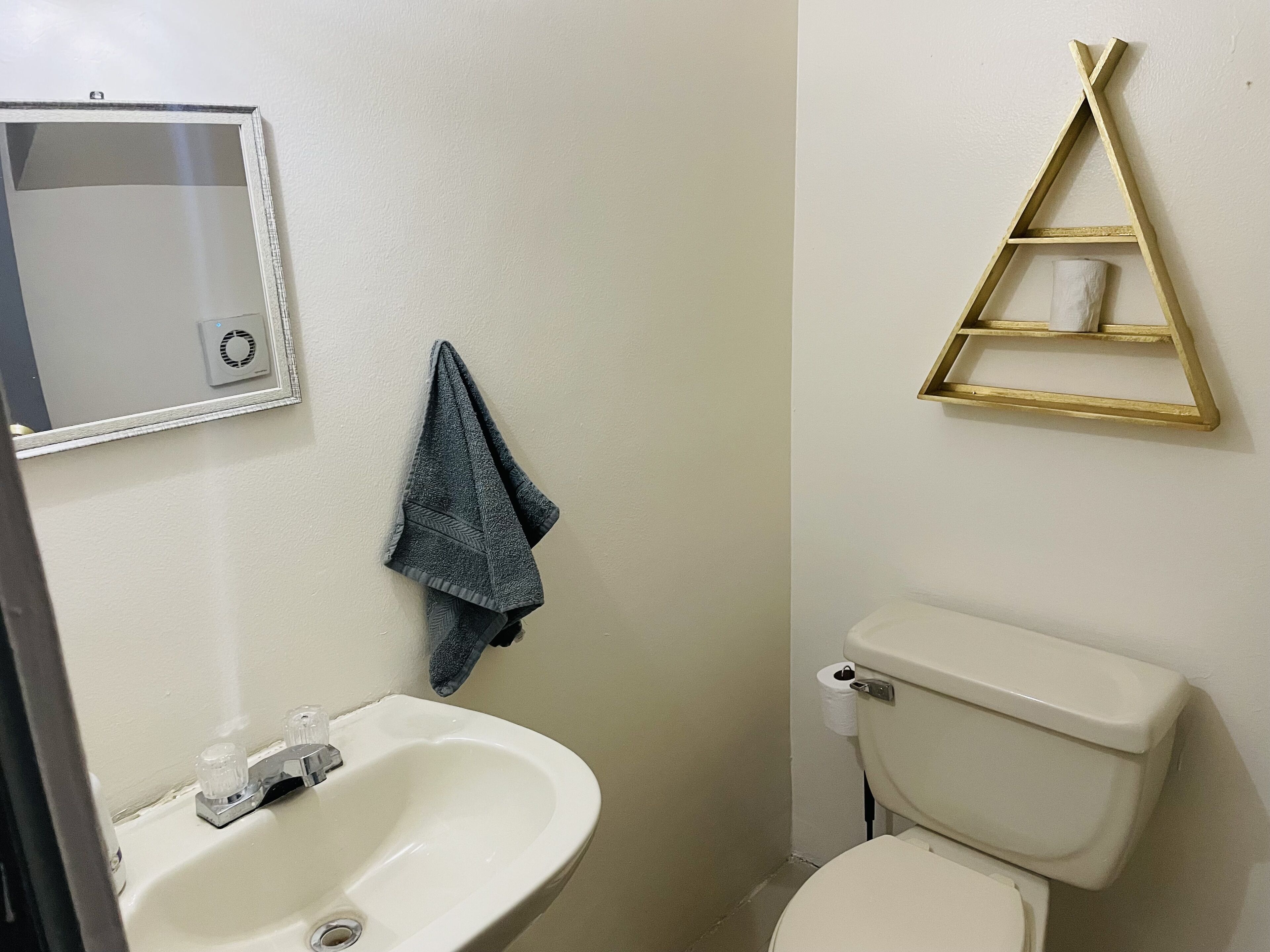 A bathroom with a white sink, a mirror, a towel hanging on the wall, and a toilet with a toilet paper holder.