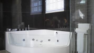 Un baño moderno con una bañera blanca grande, un cerramiento de ducha de vidrio y una pared con azulejos negros.