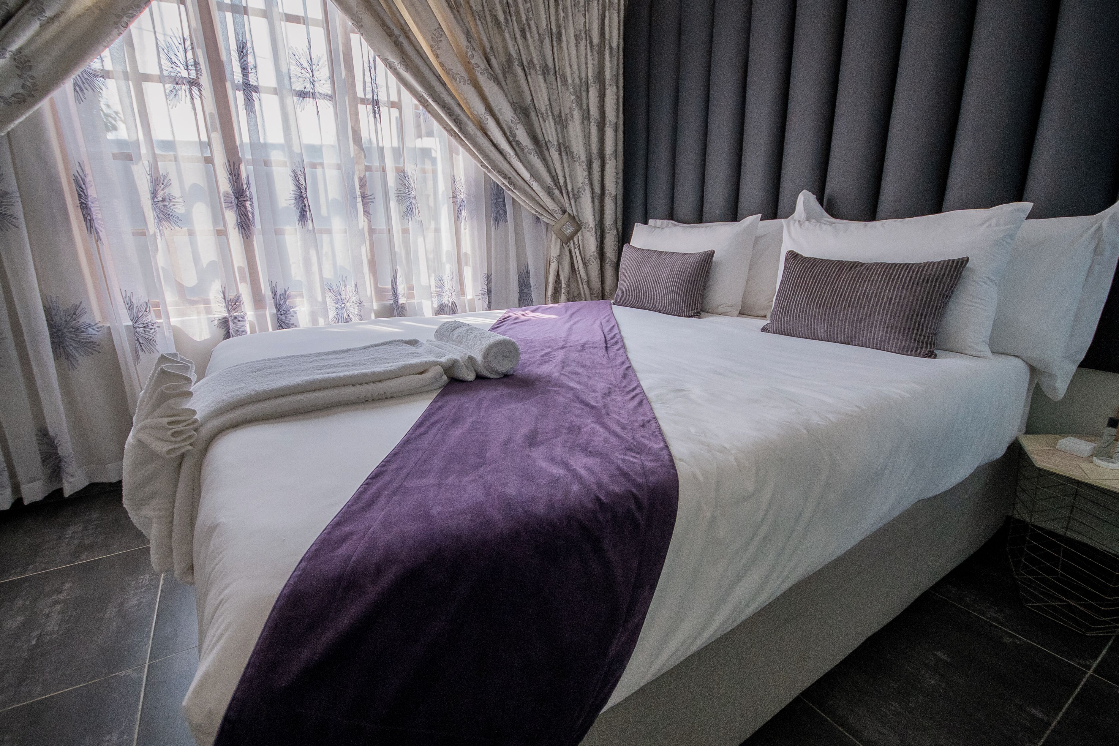 Una cama bien hecha con una manta morada, almohadas blancas y un edredón blanco.