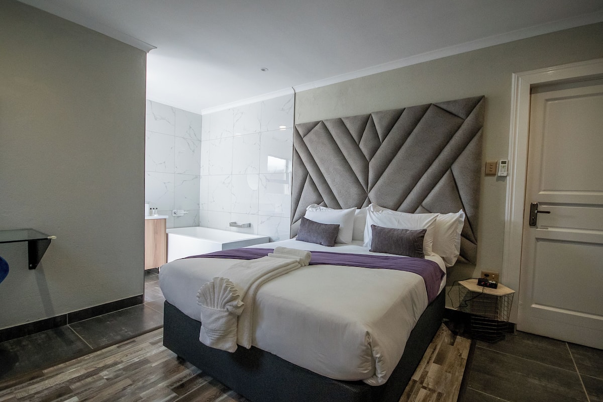 Una camera d'albergo moderna con un letto grande, un comò con uno specchio e un bagno separato.