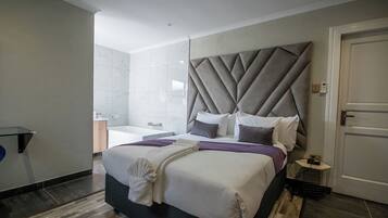 A modern hotel room with a large bed, a vanity with a mirror, and a separate bathroom.