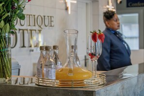 Uma área de recepção de hotel com uma vitrine de vidro contendo uma garrafa de suco de laranja, uma garrafa de água e um copo com morango.