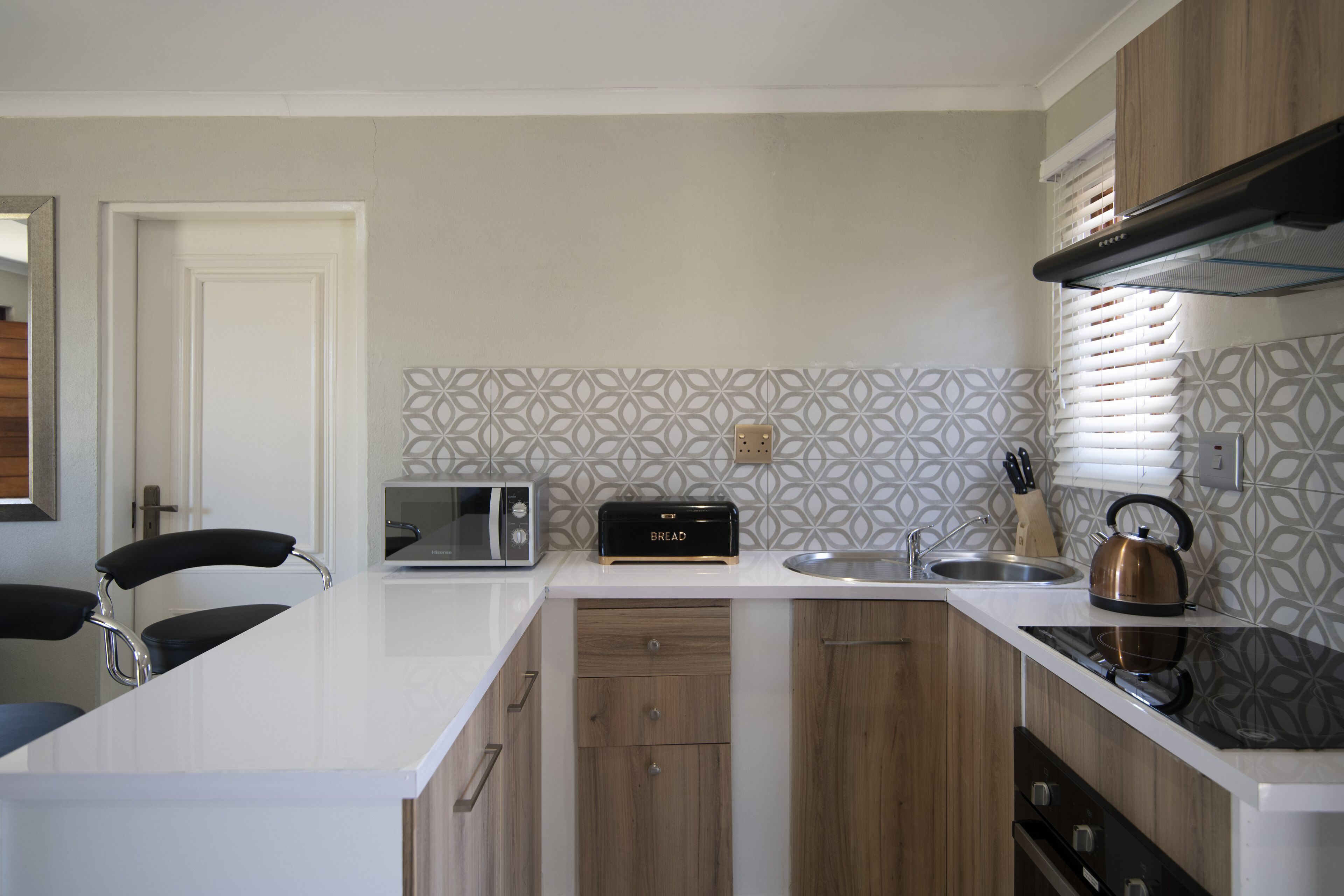 A modern kitchen with a white countertop, a built-in microwave, a toaster, a kettle, and wooden cabinets.