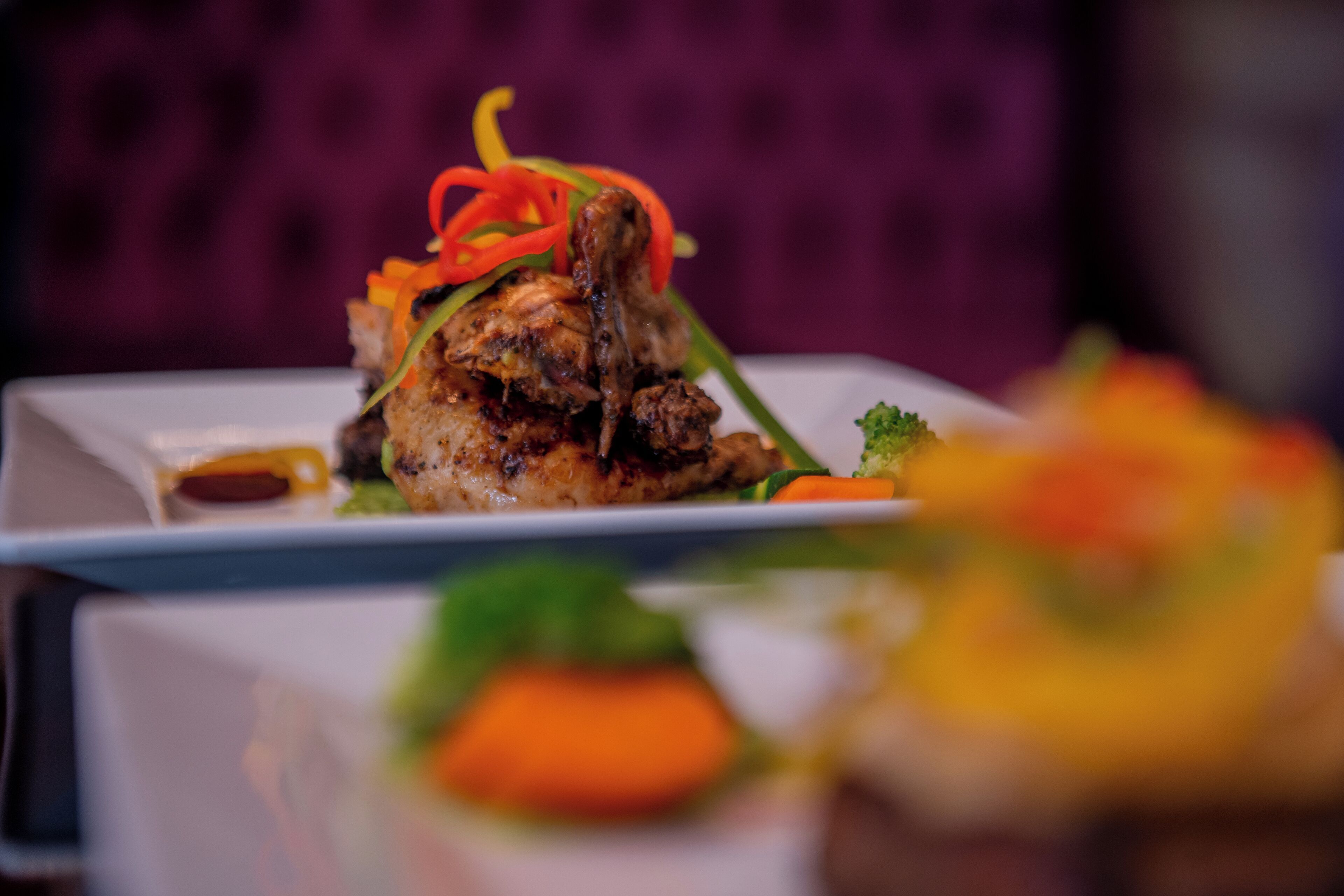 A close-up of a plated dish with grilled meat, vegetables, and sauce.