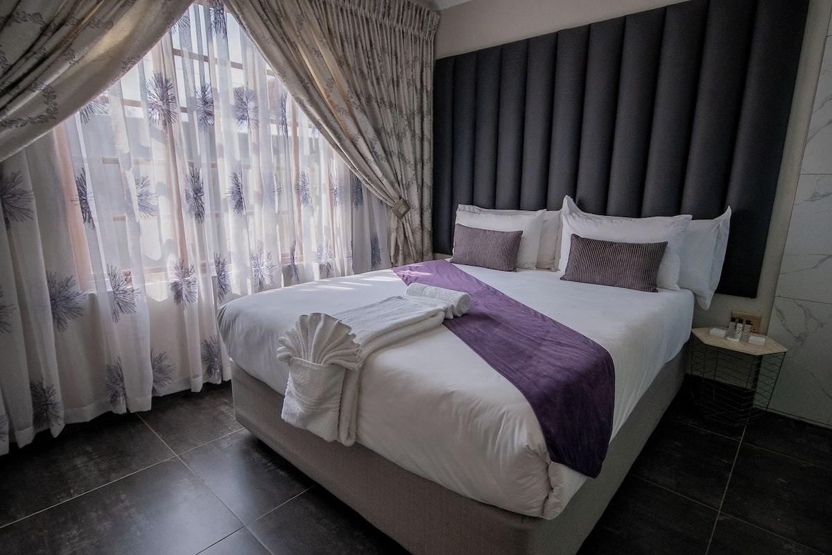 Camera d'albergo moderna con un letto grande, una testiera e un comodino.