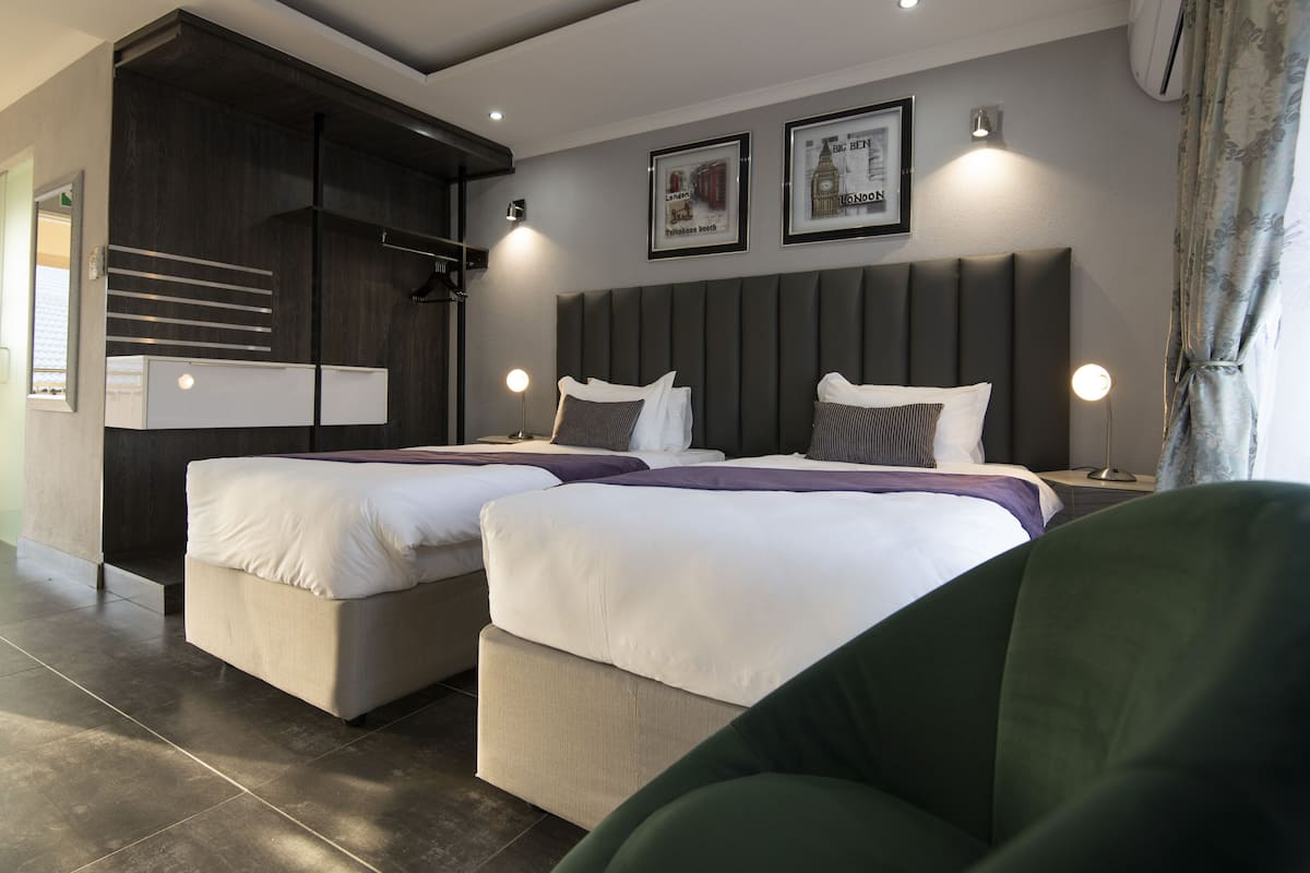 Una camera d'albergo moderna con due letti, una parete rivestita in legno scuro e quadri appesi alle pareti.