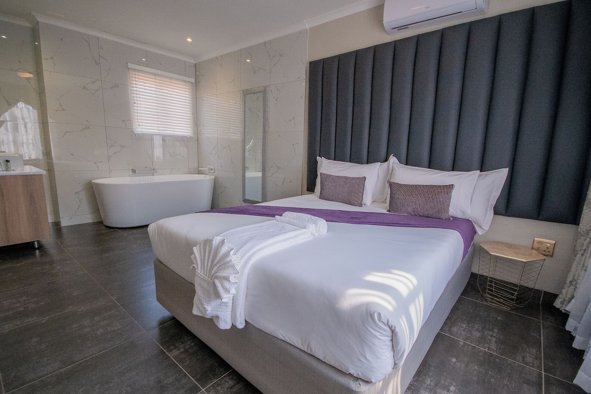 Una camera d'hotel moderna con un letto grande, bagno separato e un'ampia finestra con tende.