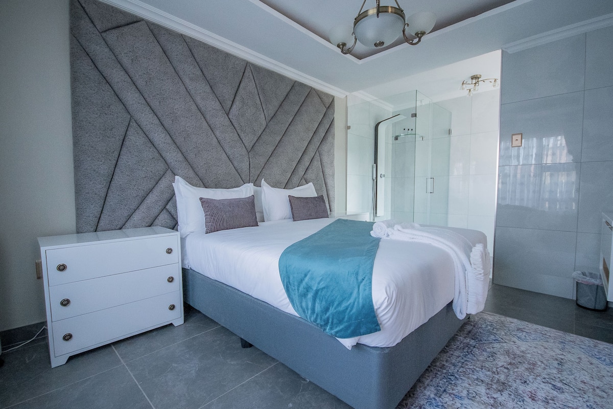 Una camera da letto moderna con un letto grande, un comodino, una testiera integrata e un box doccia in vetro.