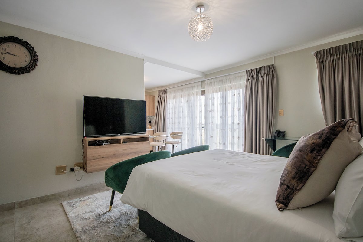 Camera d'albergo con un letto grande, una TV a schermo piatto montata a parete, una scrivania con una sedia e una finestra con tende.