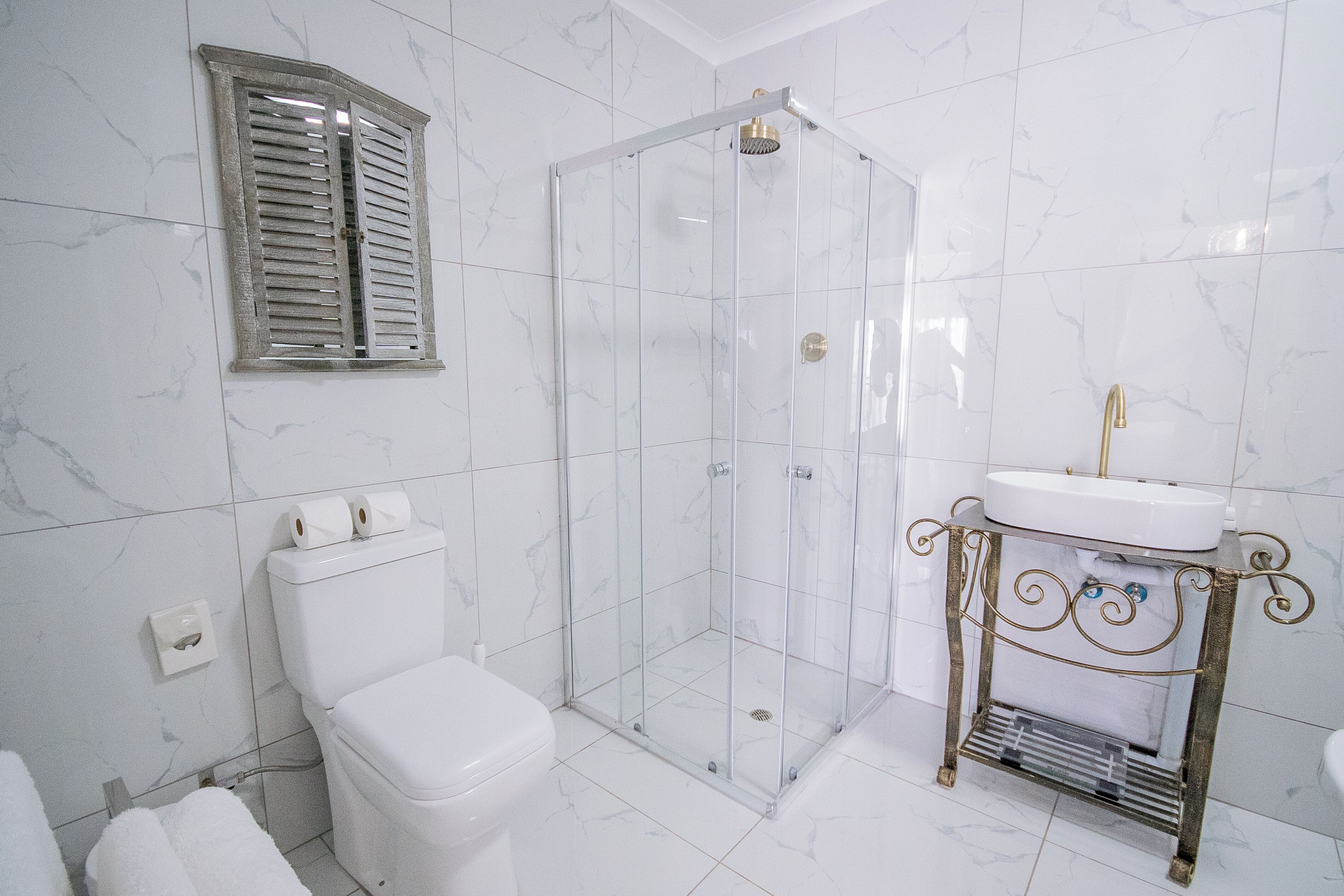 Baño con inodoro, ducha envuelta en vidrio y lavamanos con marco de metal decorativo.