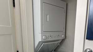 Ett kompakt, vitt tvättrum med en tvättmaskin och en torktumlare som man matar från framsidan, en dörr med ett handtag och ett litet fönster.