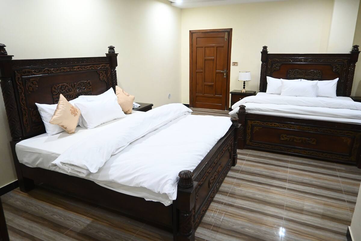 A hotel room with two wooden beds, each with white linens and decorative pillows.