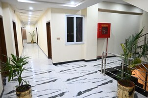 A hotel corridor with a marble floor, potted plants, a fire hose reel, and a staircase.