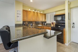 A kitchen with granite countertops, wooden cabinets, a stainless steel oven, and a black microwave.