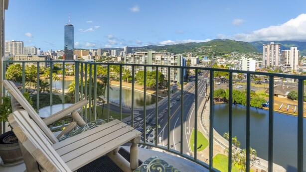 Ein Balkon mit einem Holzstuhl und Blick auf eine Stadtlandschaft, einschließlich eines Flusses und Gebäuden.
