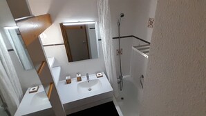 Un baño con lavamanos, espejo y ducha blancos.