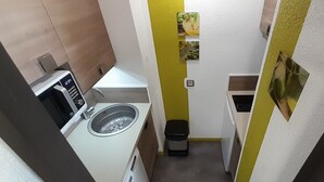 Una cocina compacta con lavadora, un pequeño bote de basura y microondas.