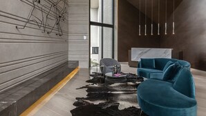 Eine moderne Lobby mit einem Marmor-Empfangstresen, einem blauen Sofa, einem Ledermatte und abstrakter Wandkunst.