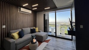 Ein modernes Wohnzimmer mit einem grauen Sofa, einem runden Beistelltisch und einem großen Fenster mit Blick auf die Stadt.