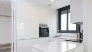 Una cocina moderna con armarios blancos, horno empotrado, hervidor de acero inoxidable y ventana sobre el fregadero.